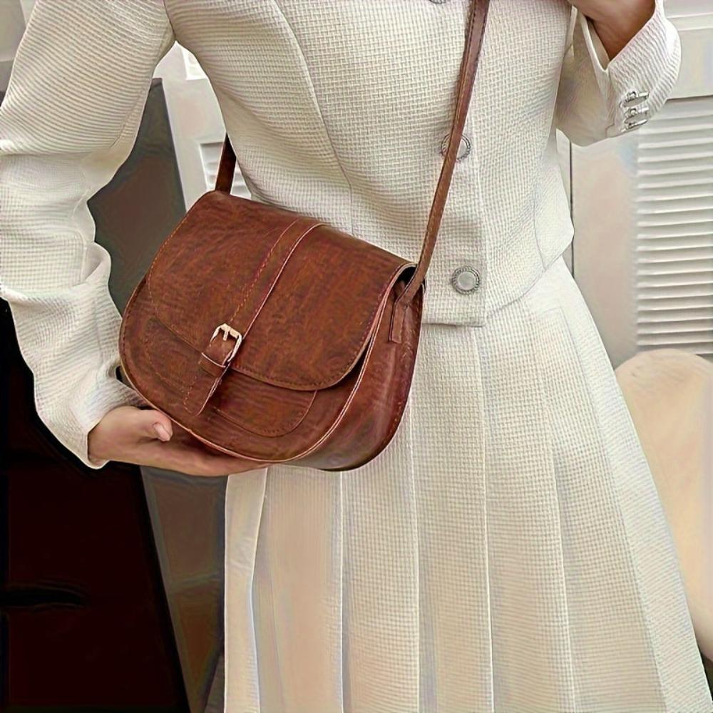 A woman carrying a crossbody satchel at her hip while out for a walk in town.
