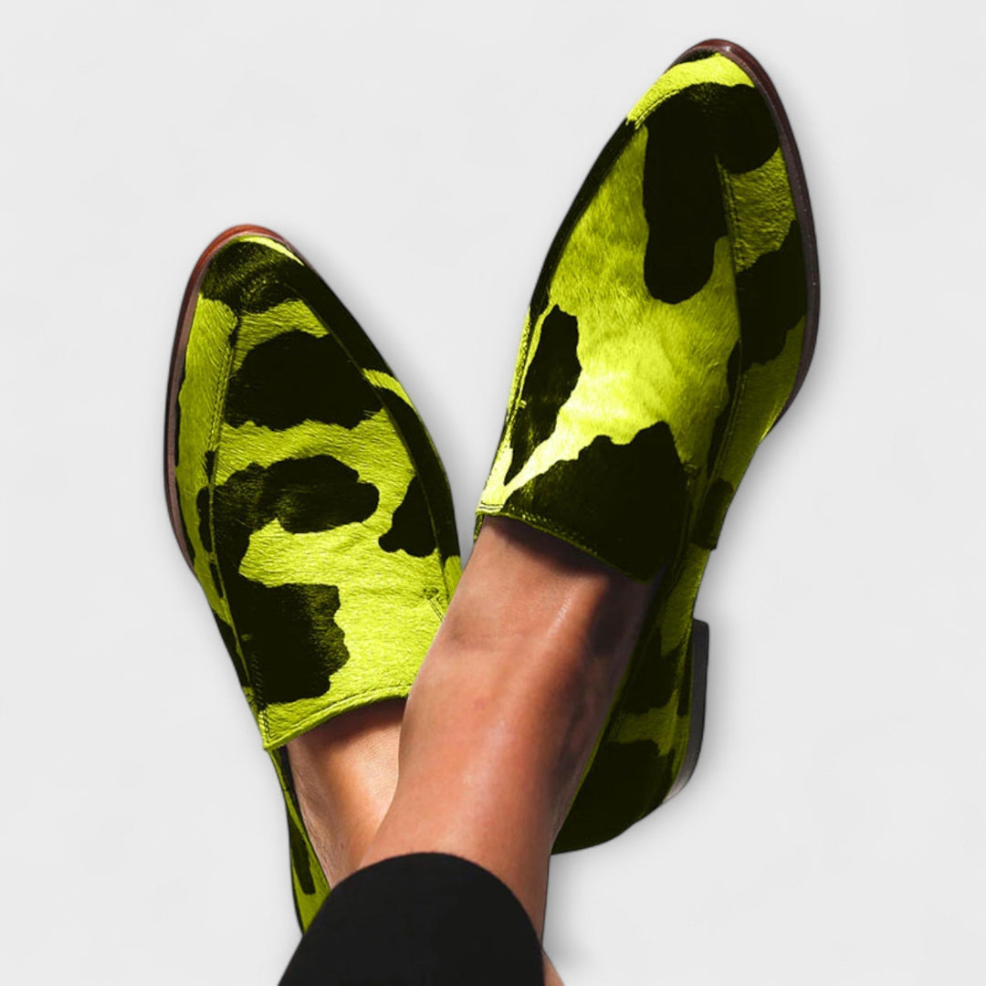 A woman wearing green cow print slip-on loafers, styled for an easy day out.