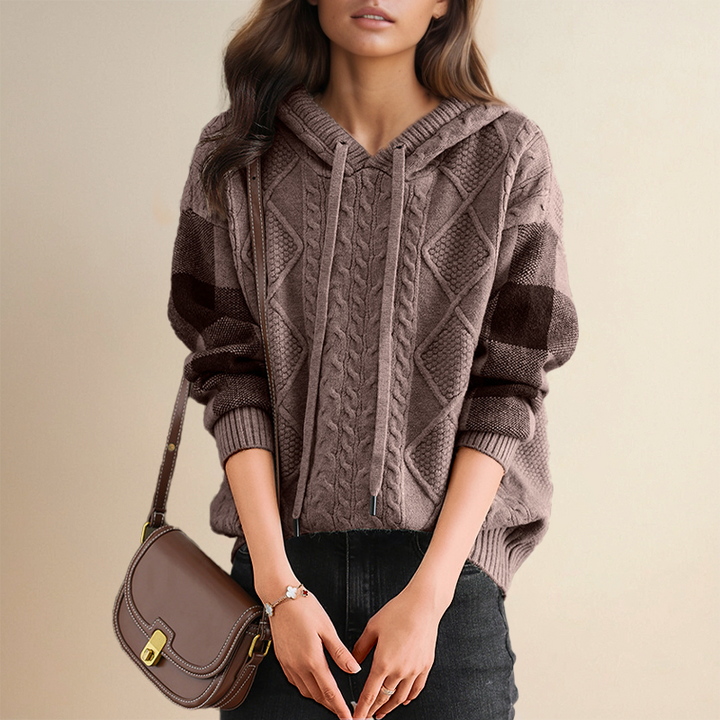 A woman wearing a soft cable-textured hooded sweater, cosy and warm with the hood down.
