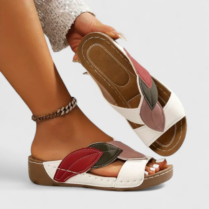 A woman wearing colourful leaf-print sandals with a cushioned insole and easy slip-on design.
