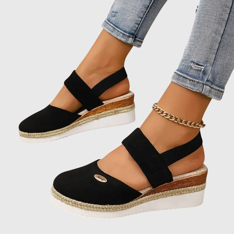 Black closed-toe wedge espadrilles with a wide stretch strap and a braided-trim platform wedge.