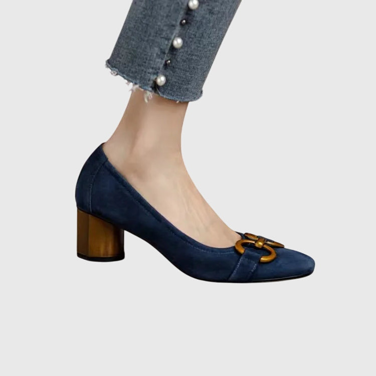 A woman wearing khaki block-heel court shoes with a gold buckle detail, standing with ease and confidence.