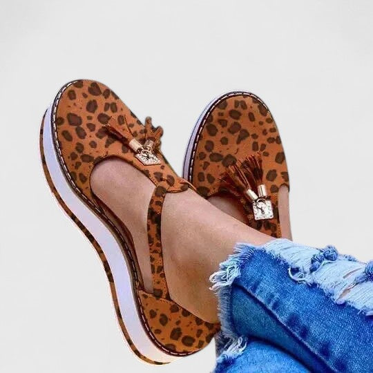 A woman wearing elegant supportive loafers with golden detail and tailored pants, looking polished and at ease.