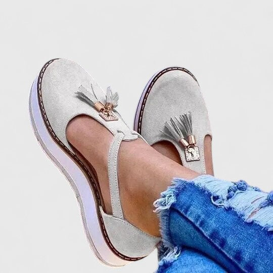 A woman wearing elegant supportive loafers with golden detail and tailored pants, looking polished and at ease.