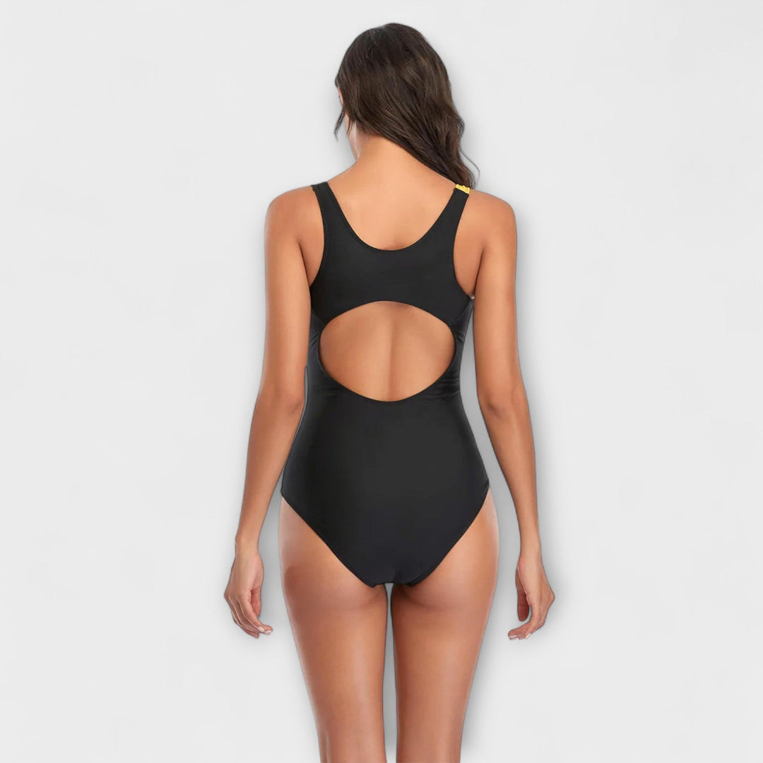 A woman by the pool in a sporty open-back swimsuit, poised and active in the sunshine.