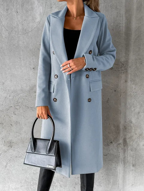 A woman wearing a long waisted coat, standing elegantly outdoors