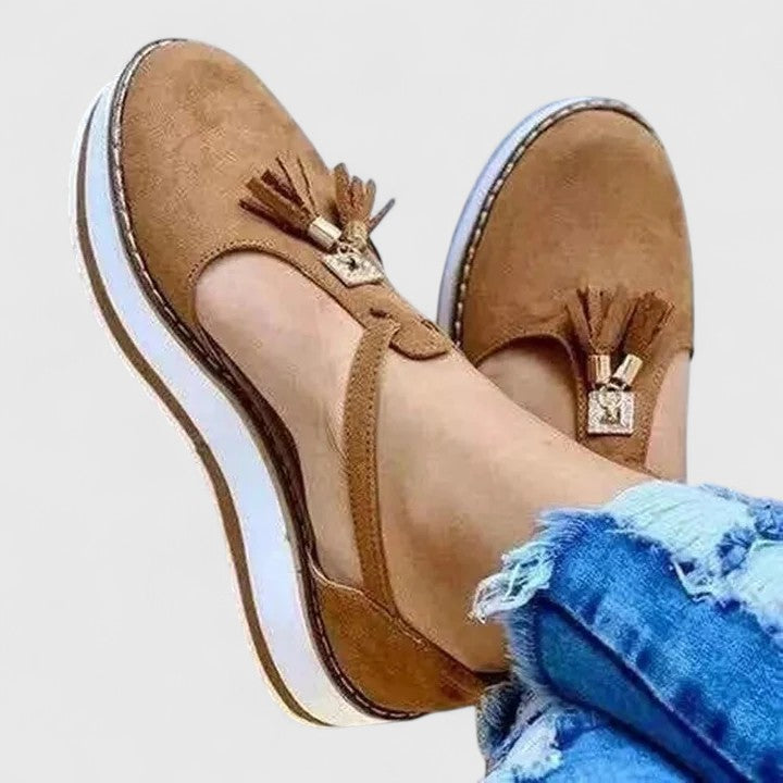 A woman wearing elegant supportive loafers with golden detail and tailored pants, looking polished and at ease.