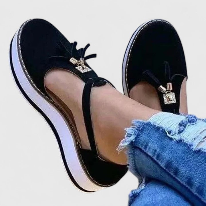 A woman wearing elegant supportive loafers with golden detail and tailored pants, looking polished and at ease.
