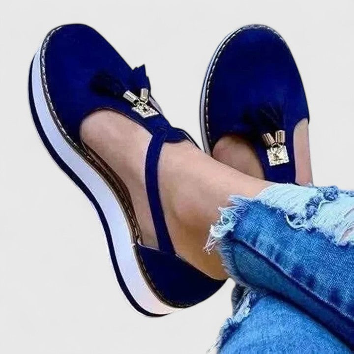 A woman wearing elegant supportive loafers with golden detail and tailored pants, looking polished and at ease.