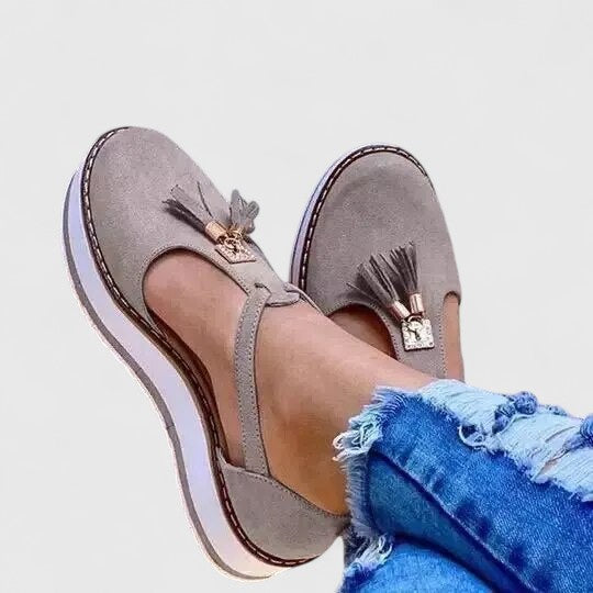A woman wearing elegant supportive loafers with golden detail and tailored pants, looking polished and at ease.