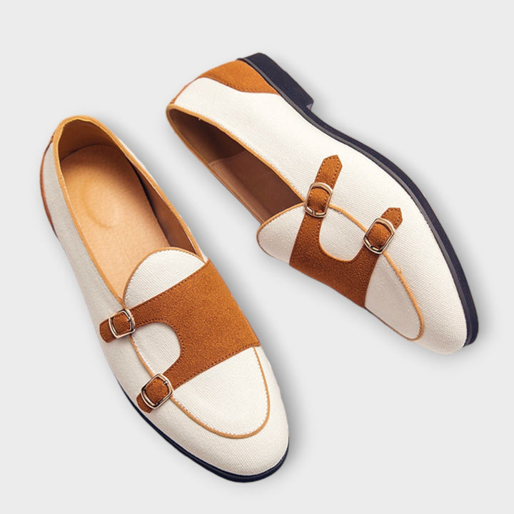 A woman wearing cream and tan round-toe slip-on loafers with twin gold buckle straps, walking with ease.