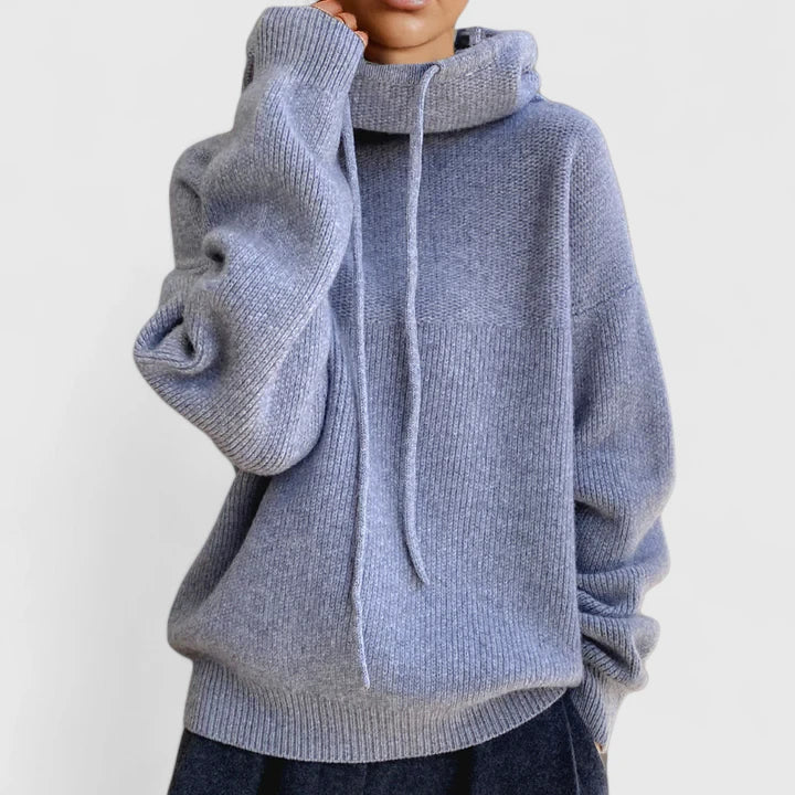 A woman wearing a cosy soft green hoodie with a drawstring hood and white pants.