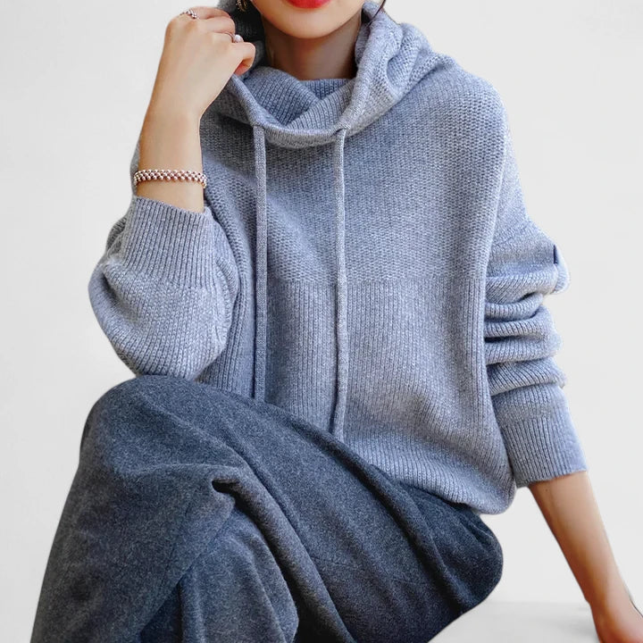 A woman wearing a cosy soft green hoodie with a drawstring hood and white pants.