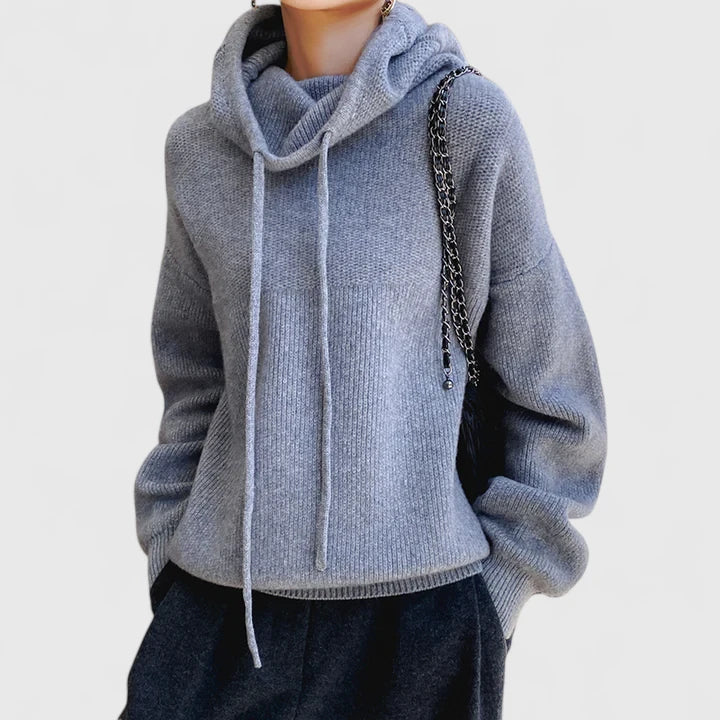 A woman wearing a cosy soft green hoodie with a drawstring hood and white pants.
