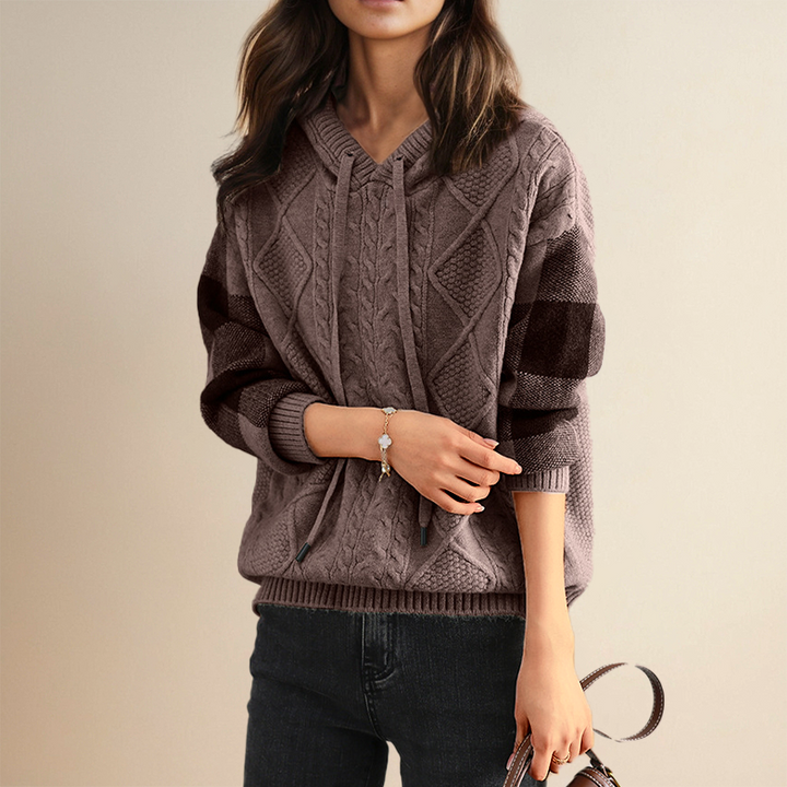 A woman wearing a soft cable-textured hooded sweater, cosy and warm with the hood down.