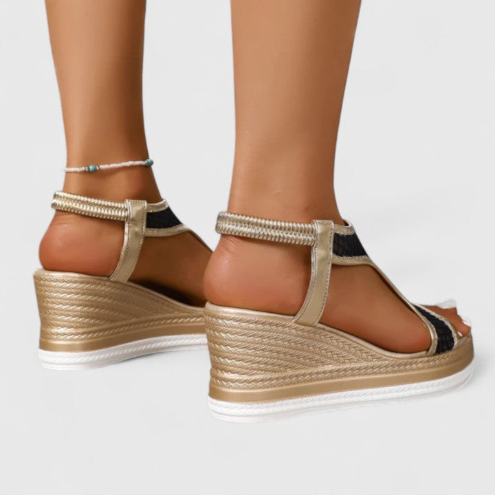 A woman wearing golden platform wedge sandals with a T-bar front, open-weave panels and a stretchy slingback.