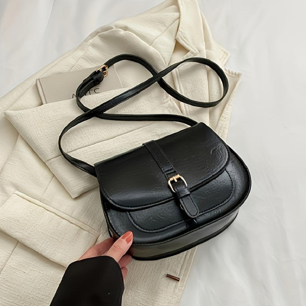 A woman carrying a crossbody satchel at her hip while out for a walk in town.