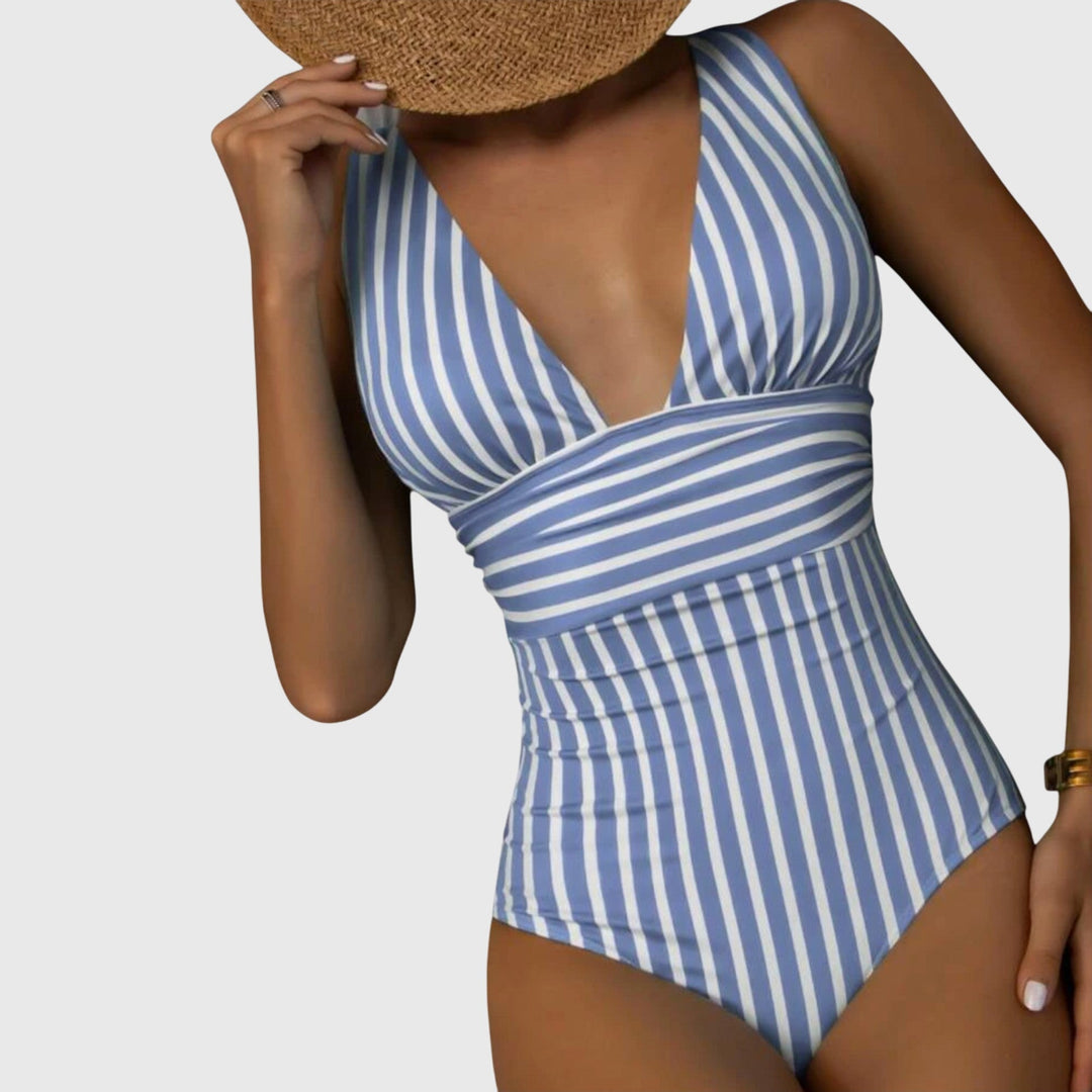 A woman by the sea in a beige and white striped V-neck swimsuit, relaxed and glowing in the sun.