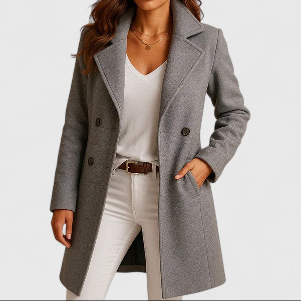 A woman wearing an elegant camel long coat with buttons, styled over jeans and boots in the city.