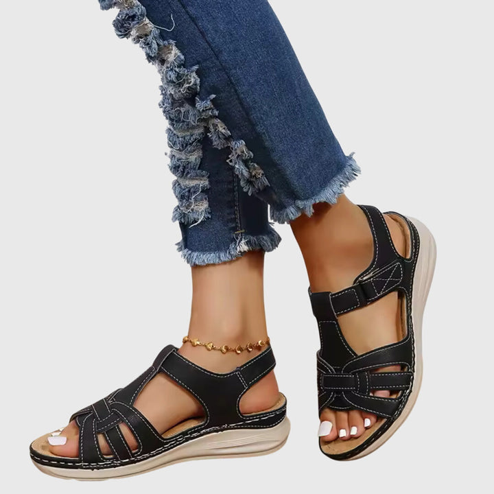 A woman wearing brown woven-effect strap sandals with a cushioned insole and adjustable strap.