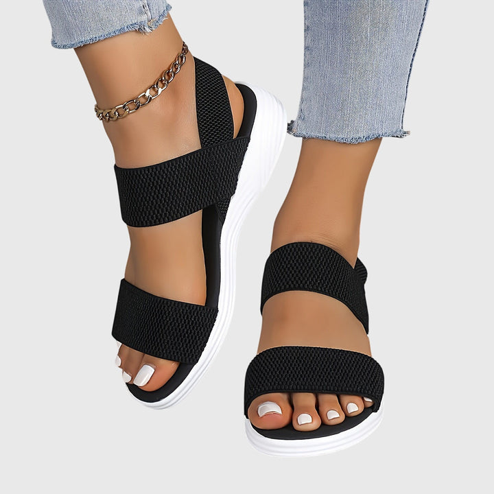 Black open-toe everyday sandals with wide stretch straps and a thick cushioned sole.