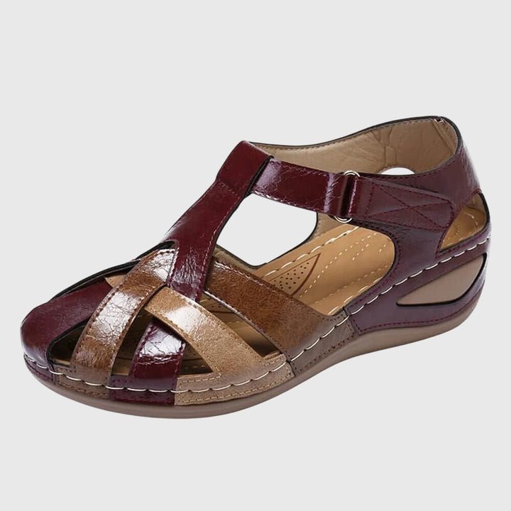 A woman wearing burgundy and brown woven closed-toe wedge sandals with side cutouts, walking with ease