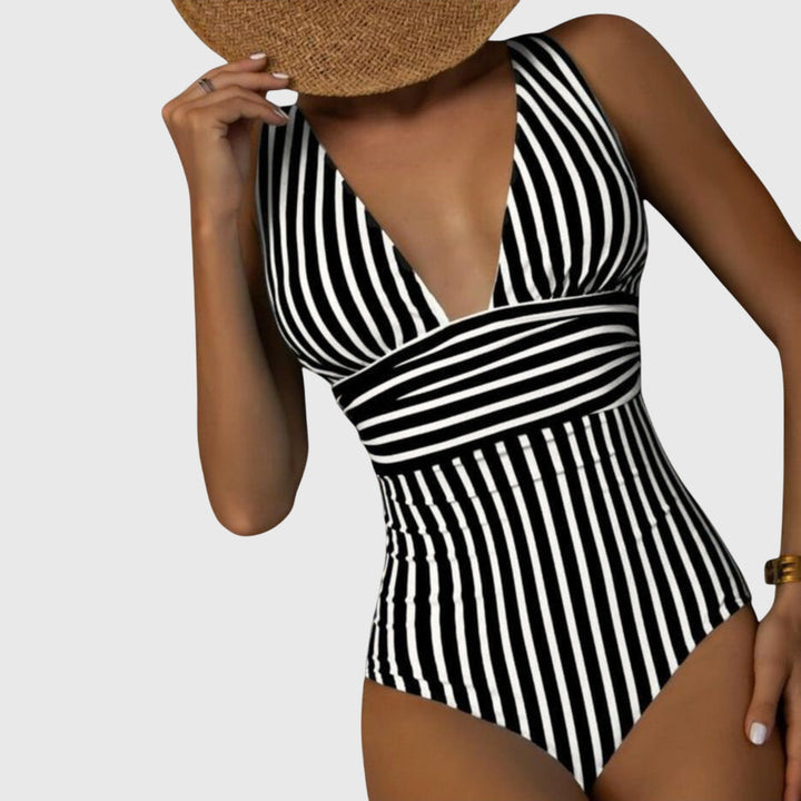 A woman by the sea in a beige and white striped V-neck swimsuit, relaxed and glowing in the sun.