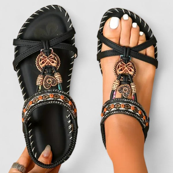A woman wearing black beaded boho sandals with braided straps, a golden medallion and a stretchy slingback.