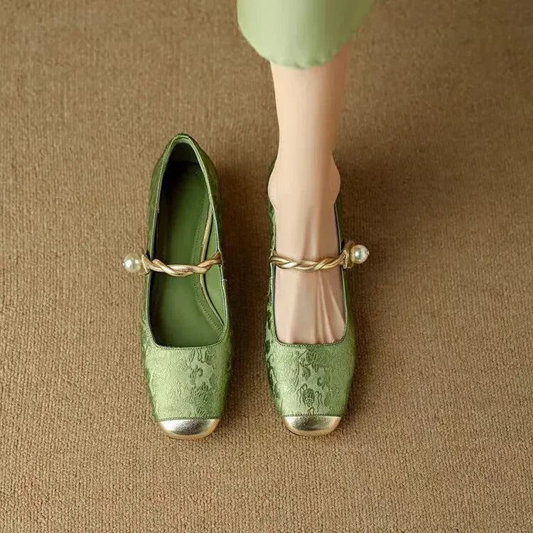 A woman wearing green low-heel Mary Janes with a twisted gold strap, gilded cap toe and a crystal-set heel