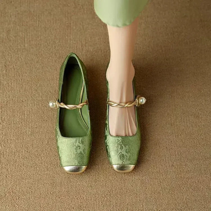 A woman wearing green low-heel Mary Janes with a twisted gold strap, gilded cap toe and a crystal-set heel