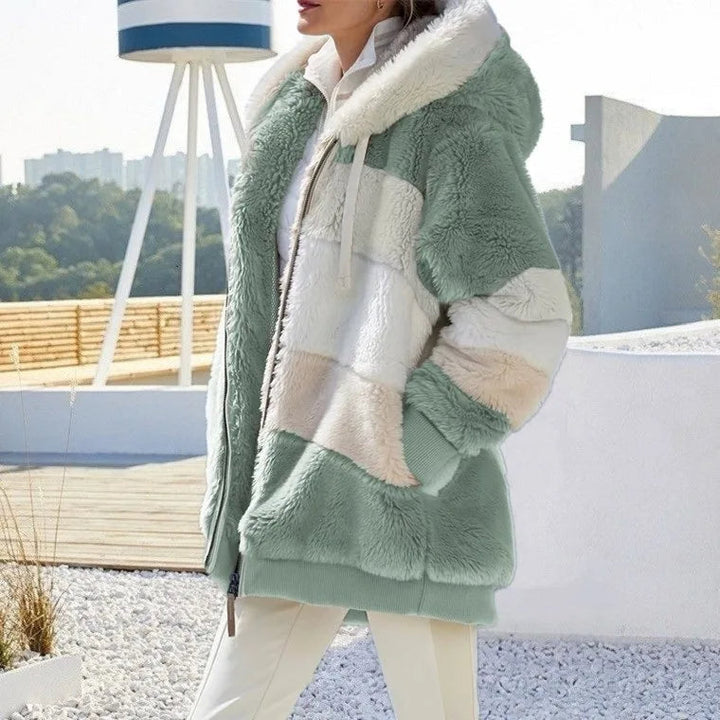 A woman wearing a plush oversized hooded zip jacket in blue and cream colour-block panels.