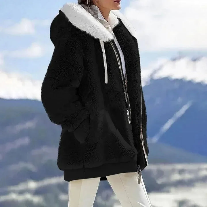 A woman wearing a plush oversized hooded zip jacket in blue and cream colour-block panels.