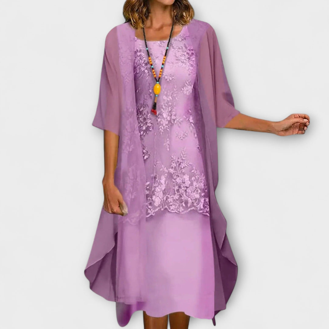 A woman wearing the Joanne layered dress in champagne, with floral embroidery, a square neckline and a sheer overlay.