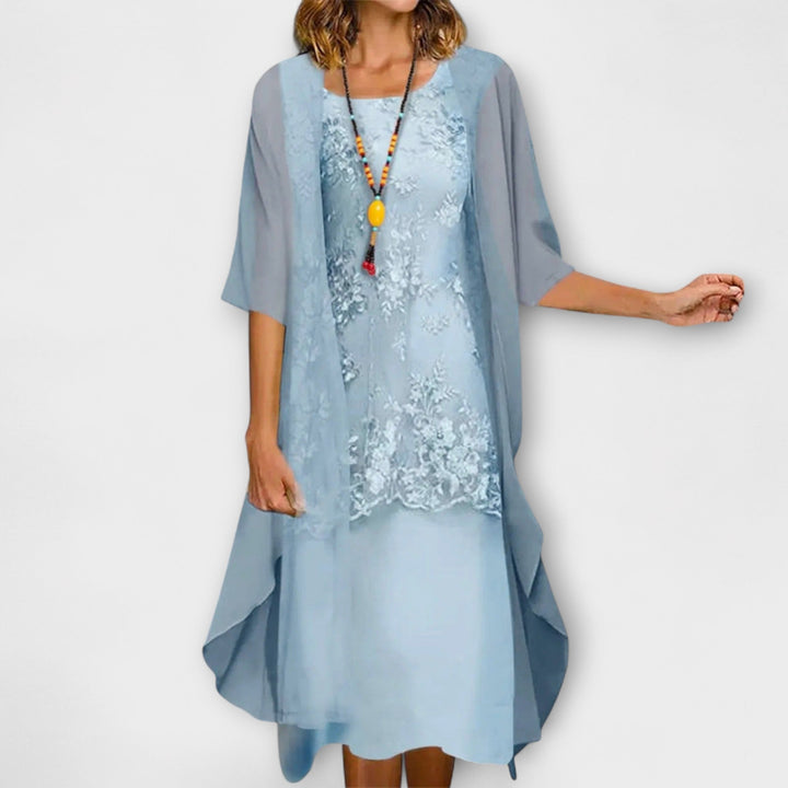 A woman wearing the Joanne layered dress in champagne, with floral embroidery, a square neckline and a sheer overlay.