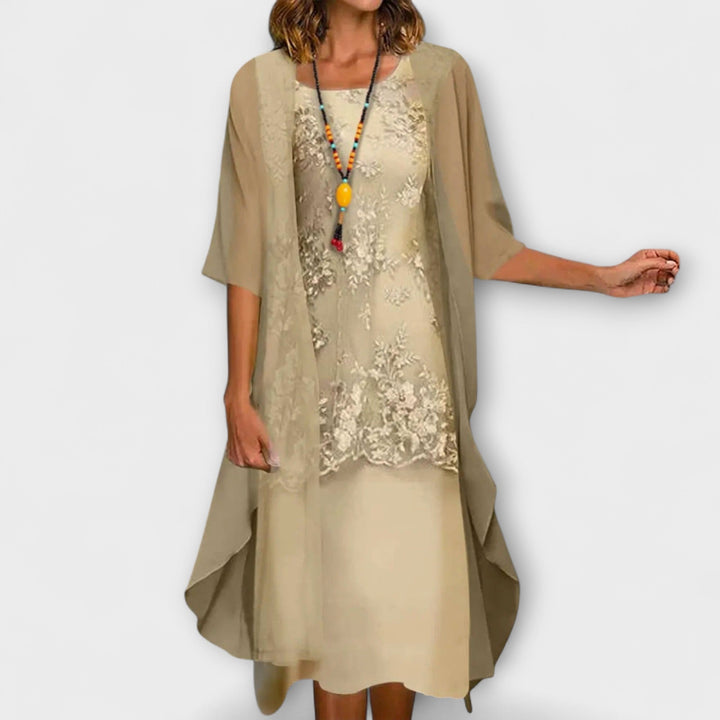 A woman wearing the Joanne layered dress in champagne, with floral embroidery, a square neckline and a sheer overlay.