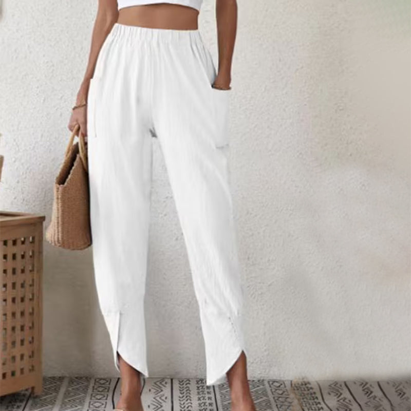 Woman wearing tapered pants with a slit hem at the ankle, walking near the coast.