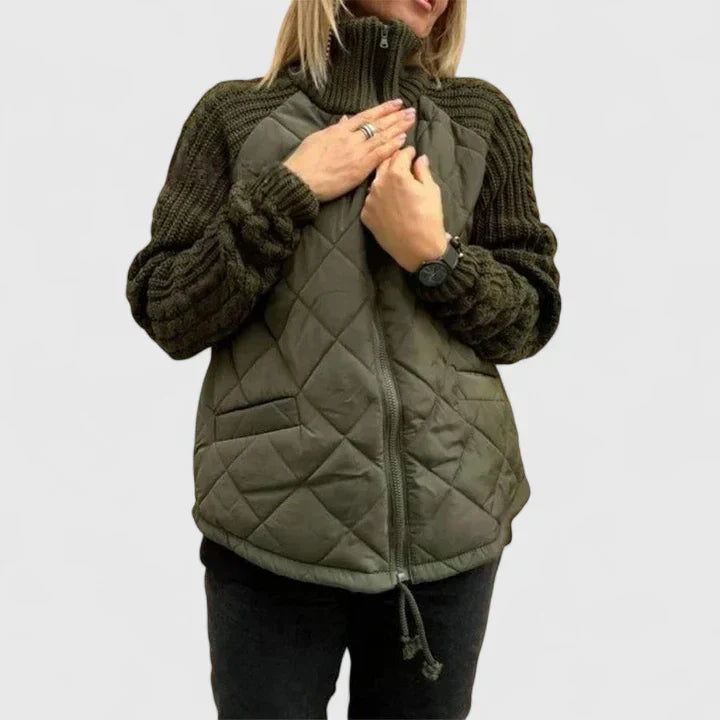 A woman wearing a light grey quilted jacket with chunky textured sleeves and a tall funnel collar.