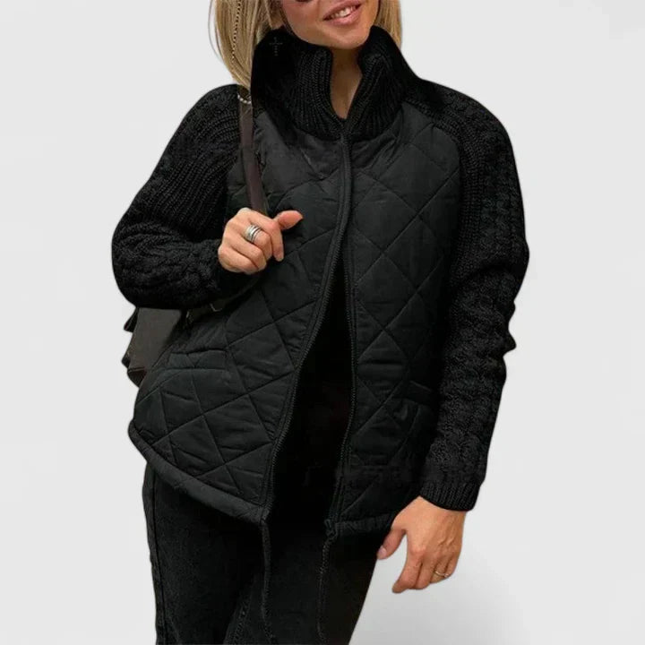 A woman wearing a light grey quilted jacket with chunky textured sleeves and a tall funnel collar.