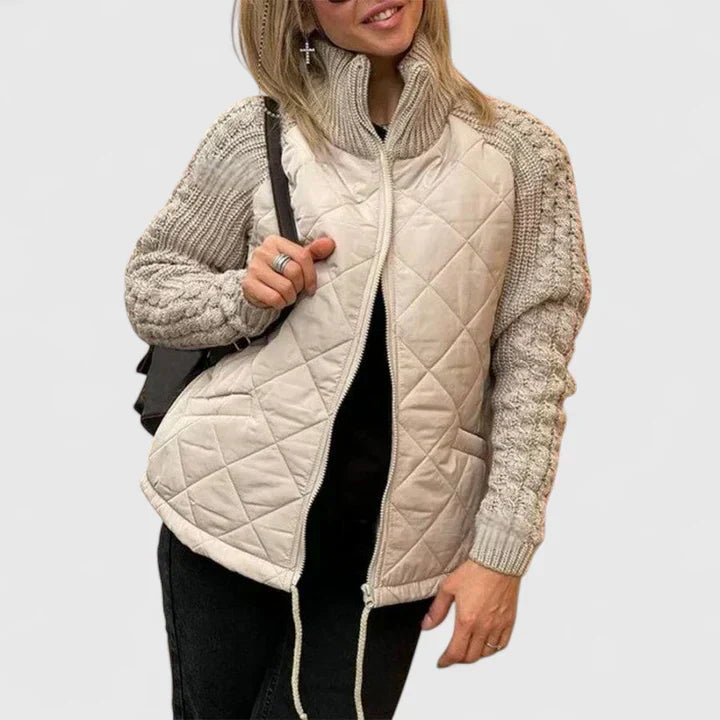 A woman wearing a light grey quilted jacket with chunky textured sleeves and a tall funnel collar.
