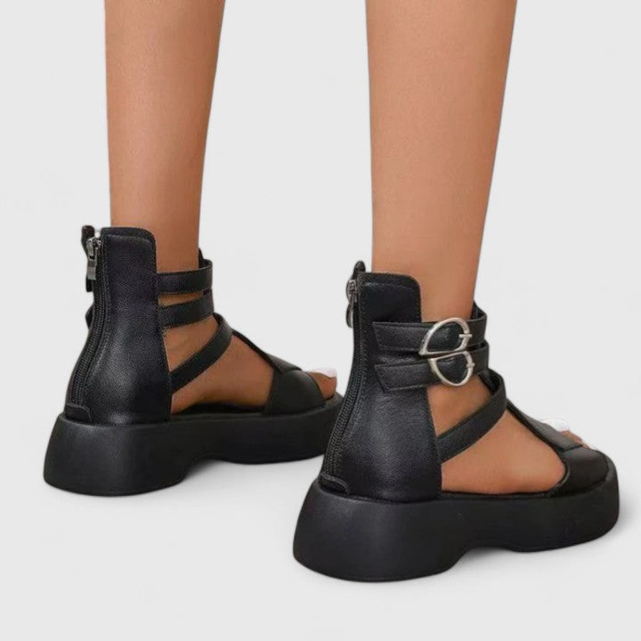 A woman stepping out in black platform sandals with crossover straps and a back zip, walking with a confident, easy stride.