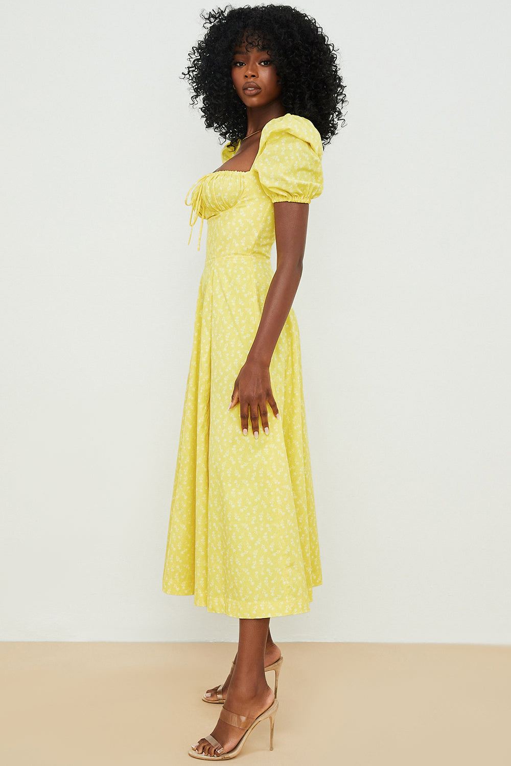 A woman wearing a floral midi dress with puff sleeves and a tie-front bodice, standing in the sunshine.