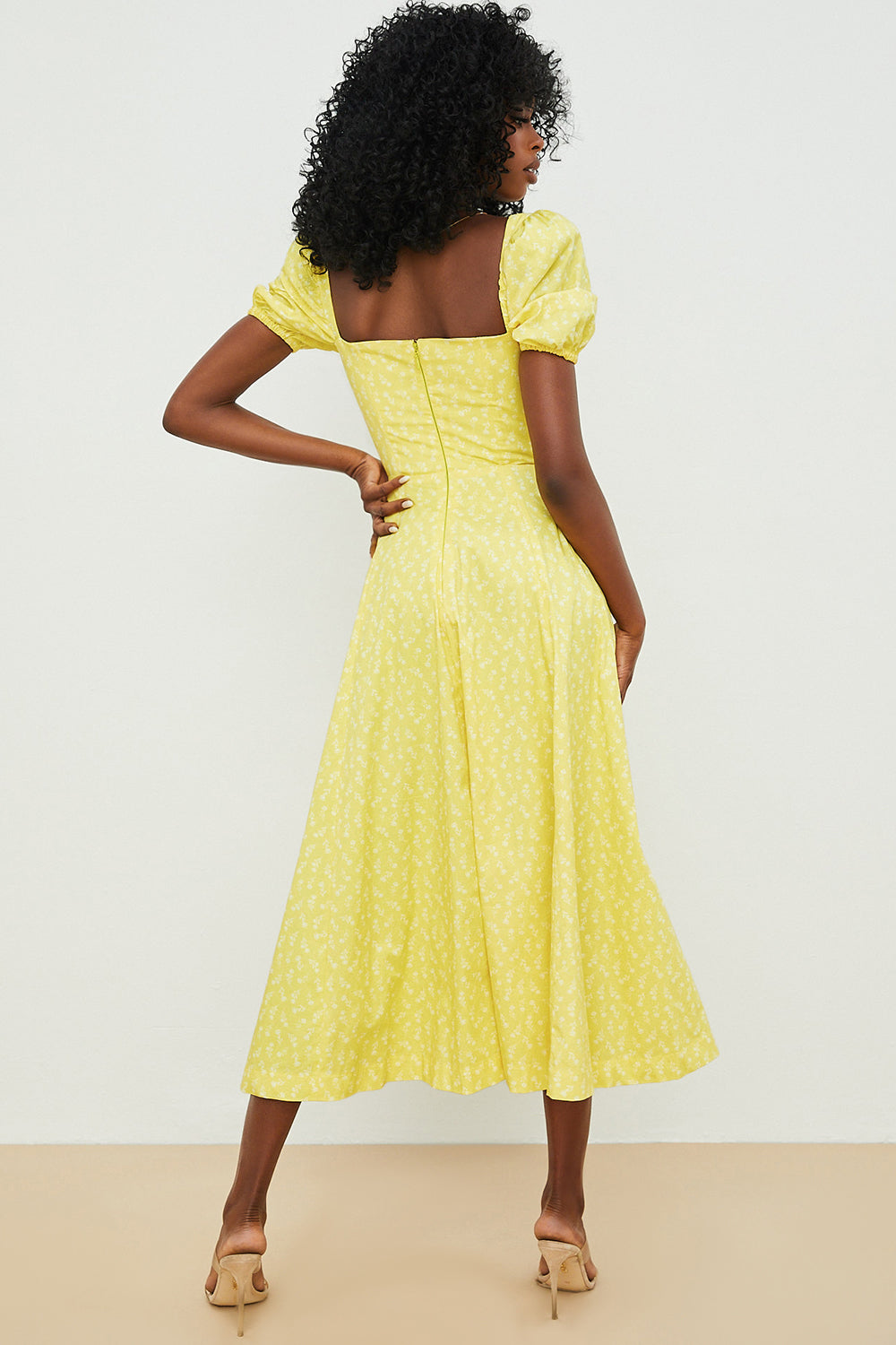 A woman wearing a floral midi dress with puff sleeves and a tie-front bodice, standing in the sunshine.