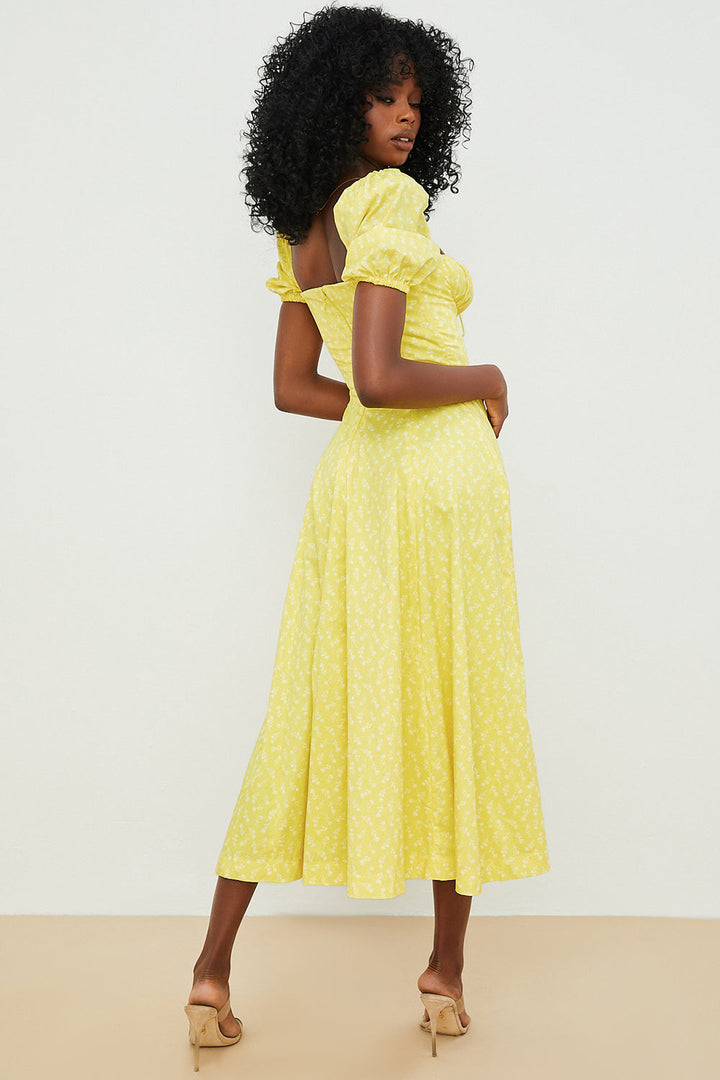 A woman wearing a floral midi dress with puff sleeves and a tie-front bodice, standing in the sunshine.