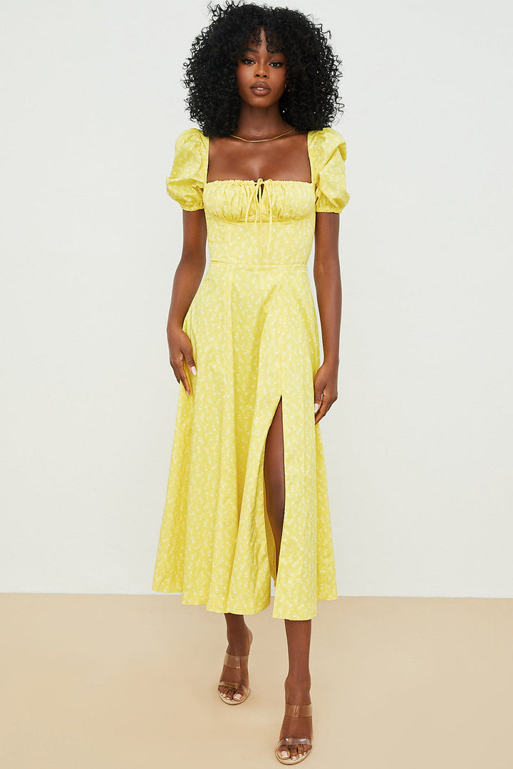 A woman wearing a floral midi dress with puff sleeves and a tie-front bodice, standing in the sunshine.