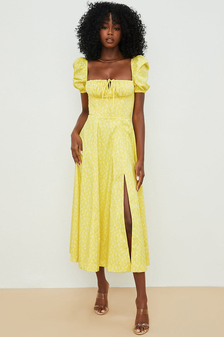 A woman wearing a floral midi dress with puff sleeves and a tie-front bodice, standing in the sunshine.
