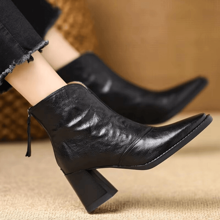 A woman in tailored pants wearing polished mid-heel ankle boots with a back zip.