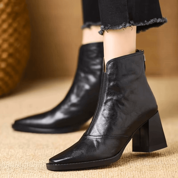A woman in tailored pants wearing polished mid-heel ankle boots with a back zip.