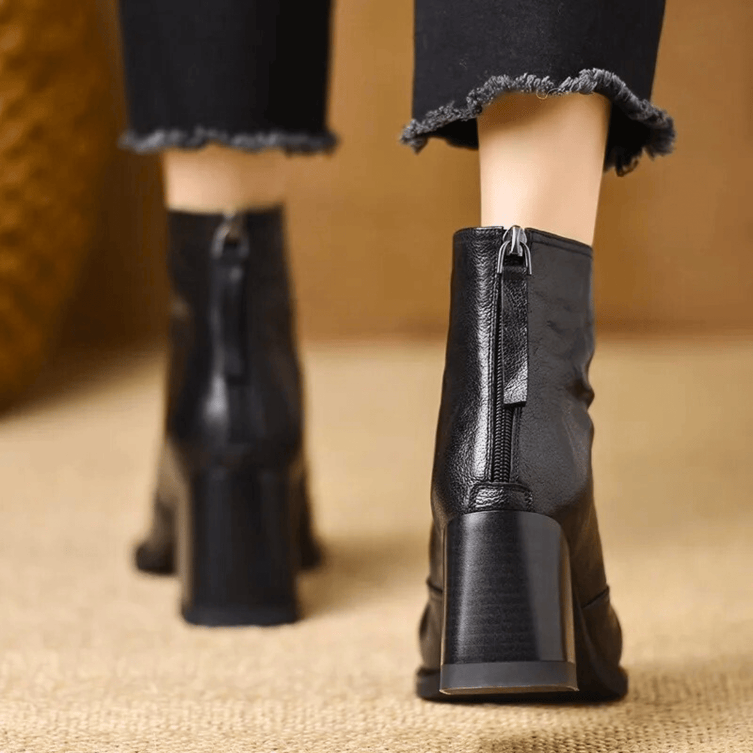 A woman in tailored pants wearing polished mid-heel ankle boots with a back zip.
