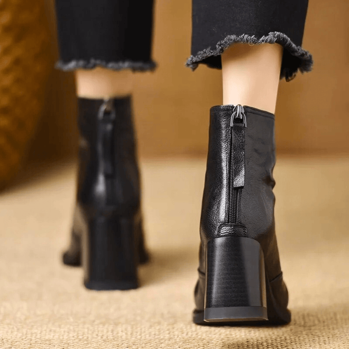 A woman in tailored pants wearing polished mid-heel ankle boots with a back zip.