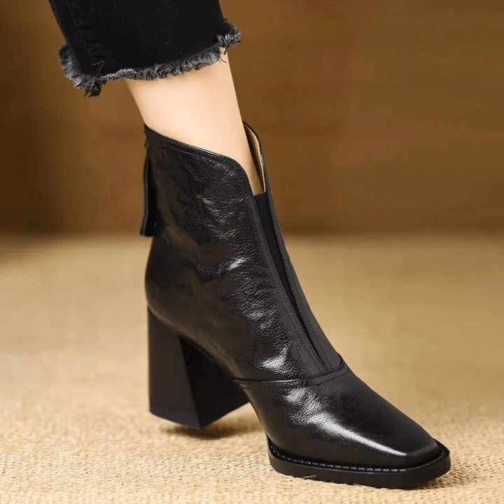 A woman in tailored pants wearing polished mid-heel ankle boots with a back zip.